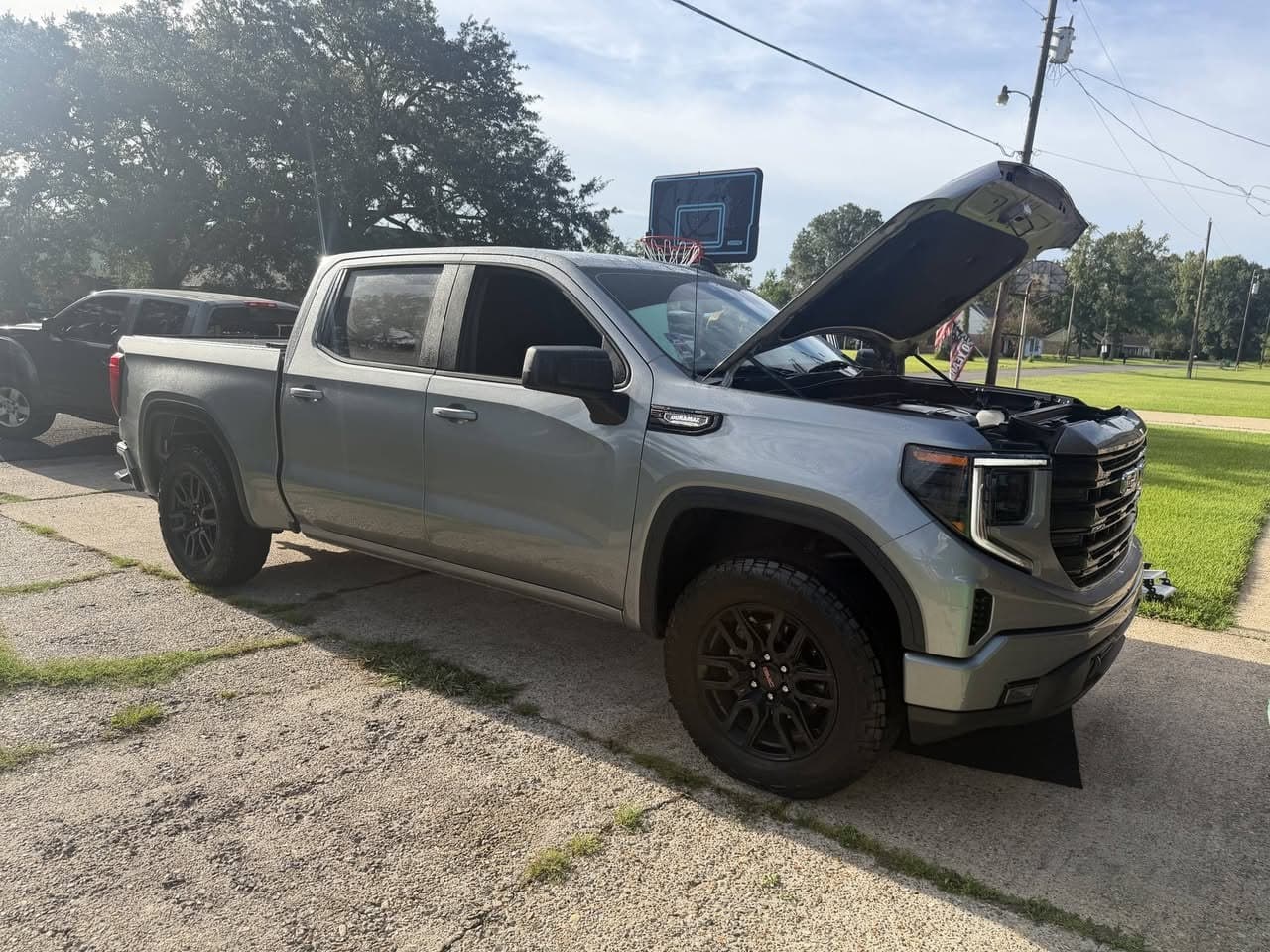 A GMC Sierra pickup with the hood up, serviced on site in a driveway rather than taken to a shop