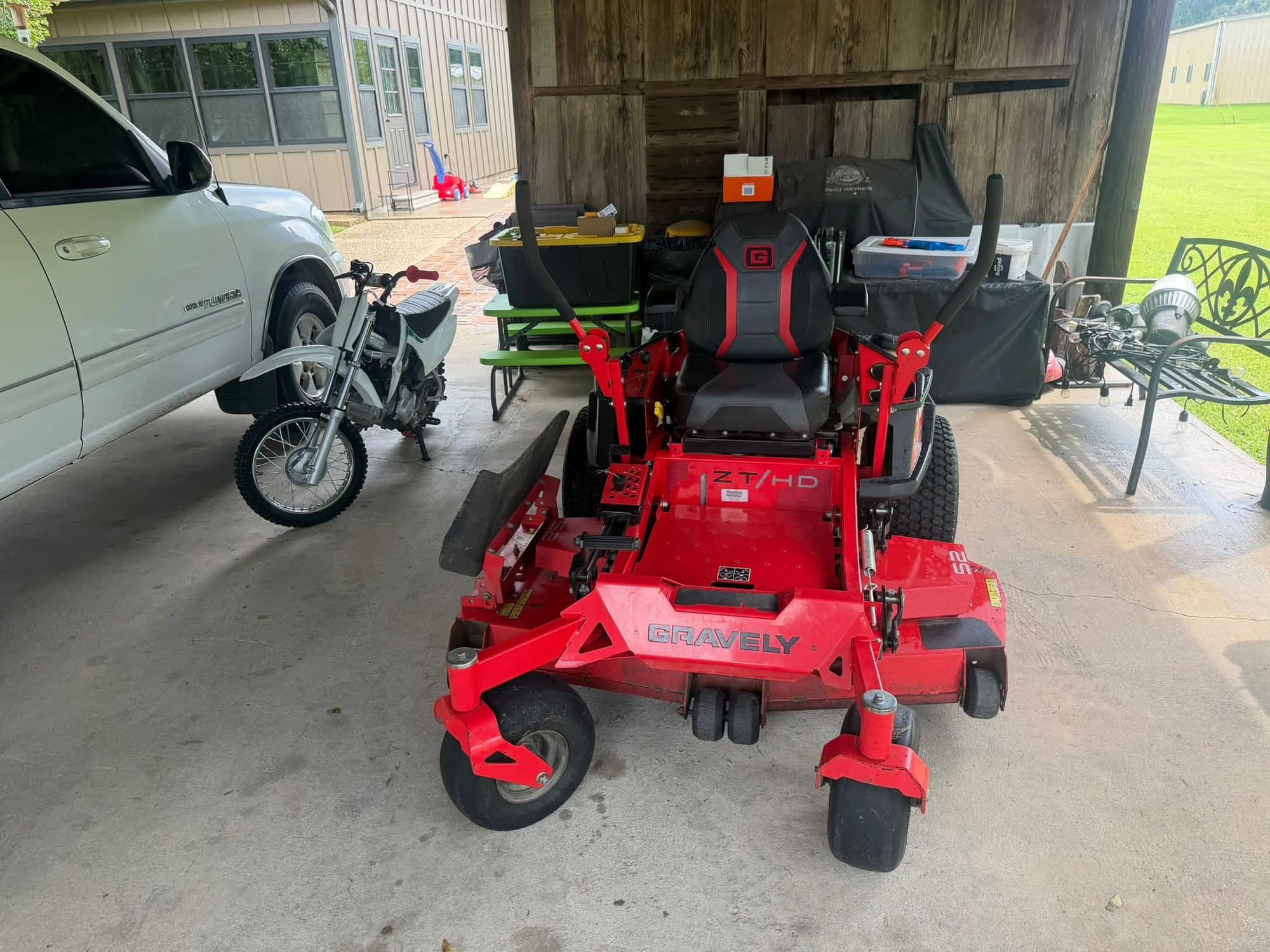 A red Gravely zero-turn mower parked in an open shed alongside other equipment, ready for a mobile service
