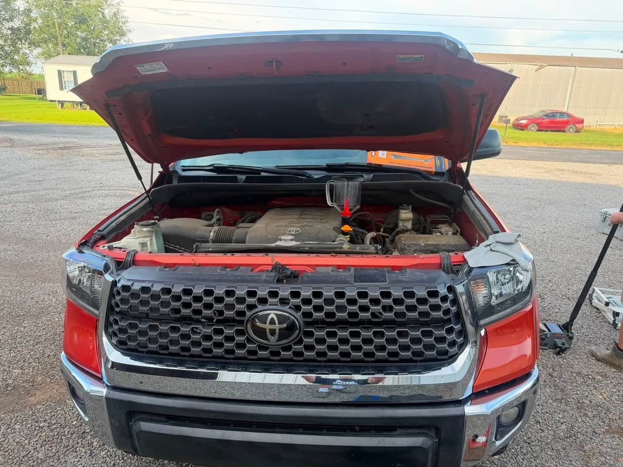 A red Toyota Tundra with the hood up in a driveway during a Bayou Boyz mobile oil change