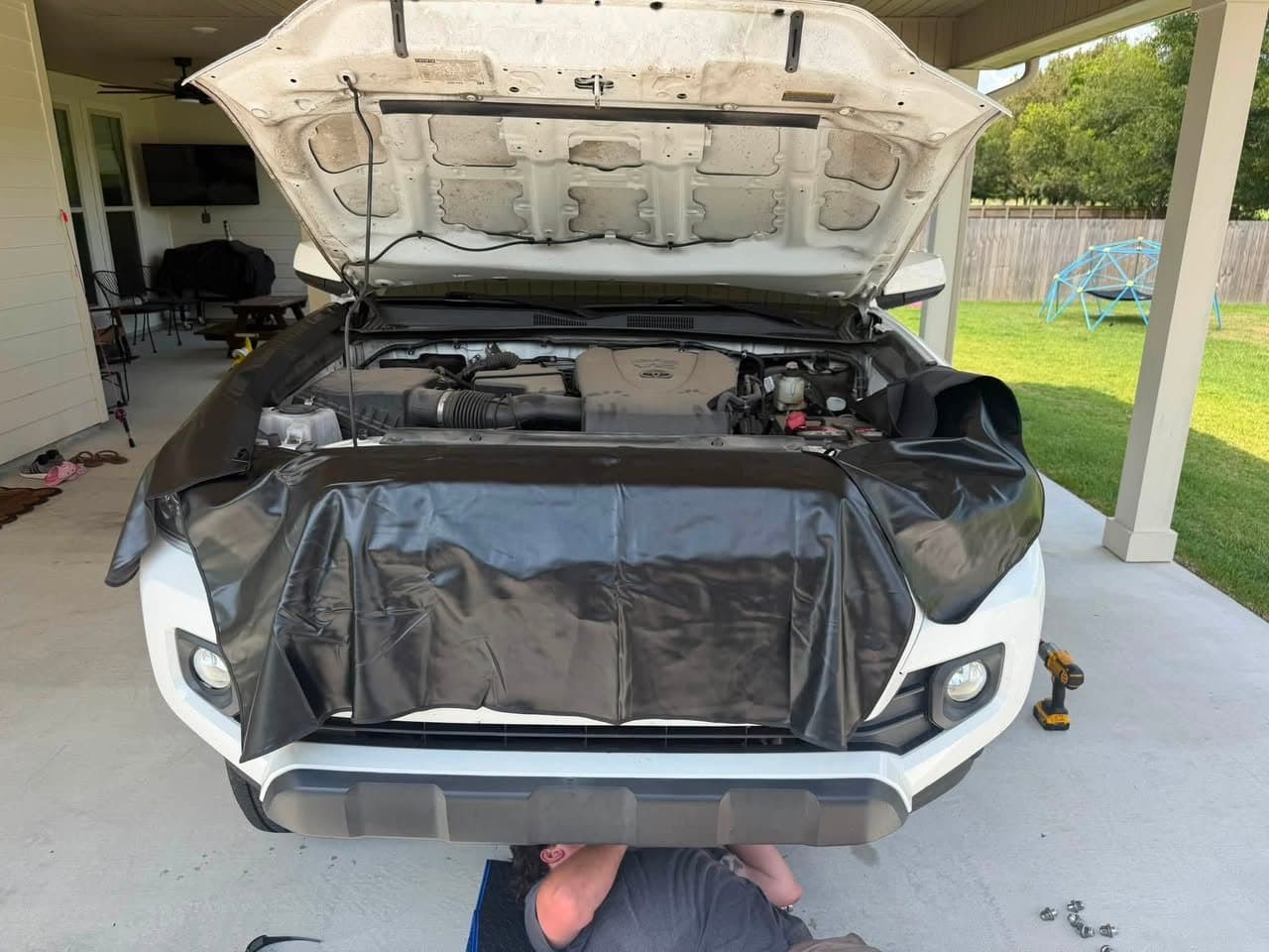 A Bayou Boyz technician working underneath a white pickup with a fender cover laid over the grille